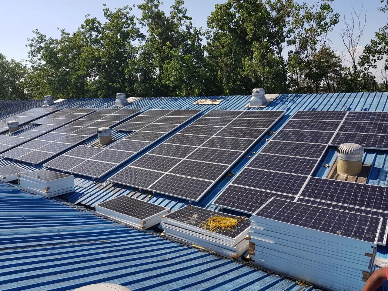 Rows of solar modules around roof ventilators, with additional modules staged for installation